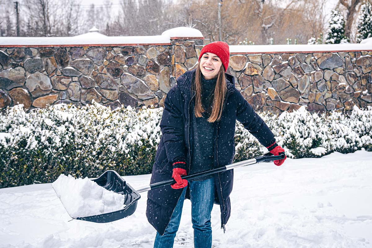 ragazza con cappello rosso spala neve nel vialetto