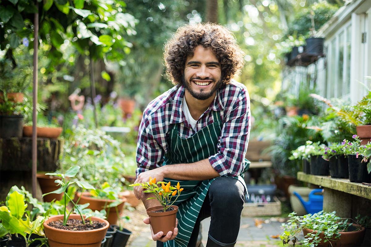 giovane ragazzo sorridente mostra piccola pianta in giardino