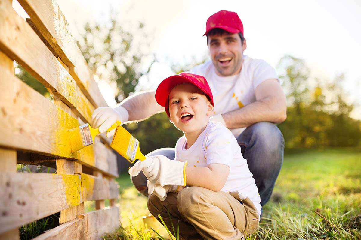 adulto e bambino pitturano staccionata di colore giallo
